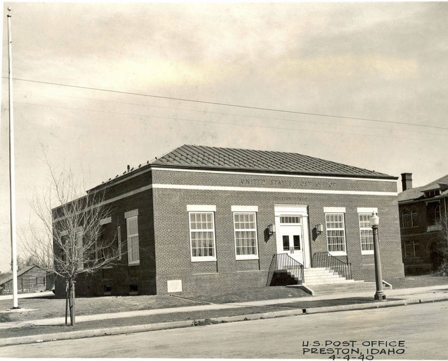 A brick building identified as the United States Post Office, with an entrance featuring double doors and a set of stairs leading up to them. The building has large windows and a lamp post near the entrance. A bare tree and a pole are visible in front. The text "U.S. Post Office, Preston, Idaho, 4-4-40" is written at the bottom.