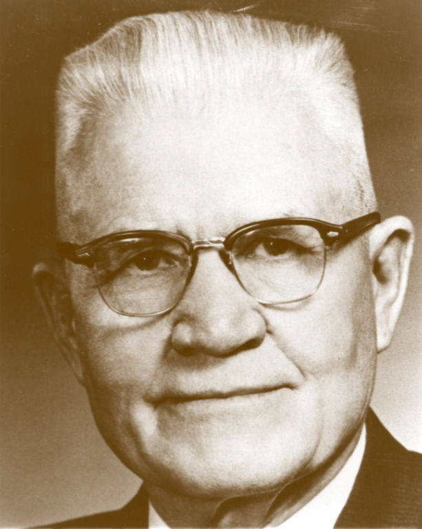 An older man wearing glasses with short, neatly combed hair. He is looking directly at the viewer with a neutral expression.