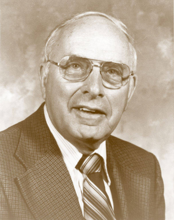 An older man wearing glasses and a suit jacket with a striped tie.