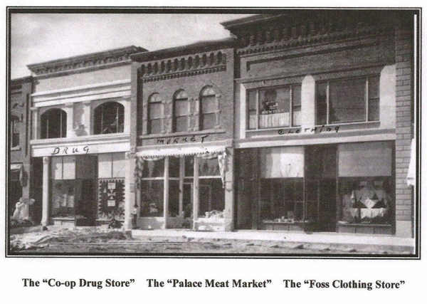Three storefronts are visible in a row. The first is labeled "DRUG," the second is labeled "MARKET," and the third is labeled "CLOTHING." Below the image, there are captions for each store, reading: "The 'Co-op Drug Store,'" "The 'Palace Meat Market,'" and "The 'Foss Clothing Store.'"