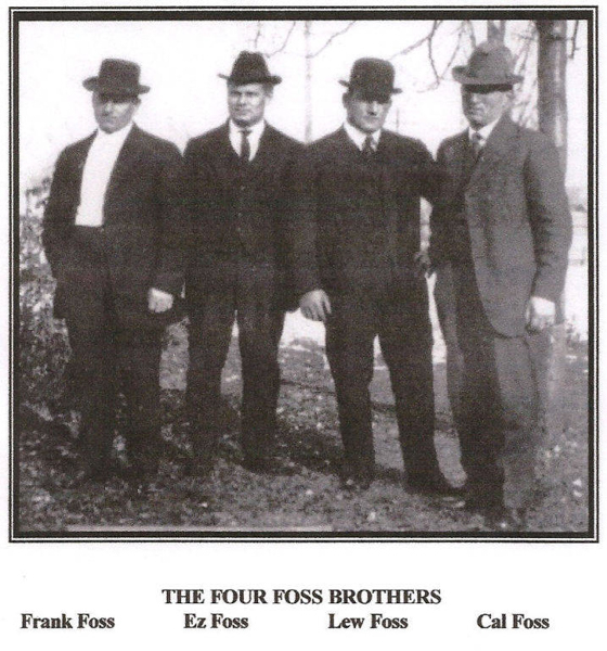 Four men are standing side by side outdoors, all wearing suits and hats. Below them, there is text that reads: "THE FOUR FOSS BROTHERS." Underneath, each man's name is listed: Frank Foss, Ez Foss, Lew Foss, and Cal Foss.