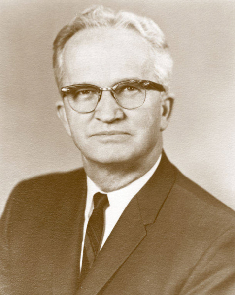 An older man with glasses, short white hair, and a serious expression, wearing a suit and tie.