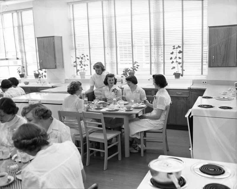 Multiple groups of women sitting down at their respective tables to dine in Home Economics class.