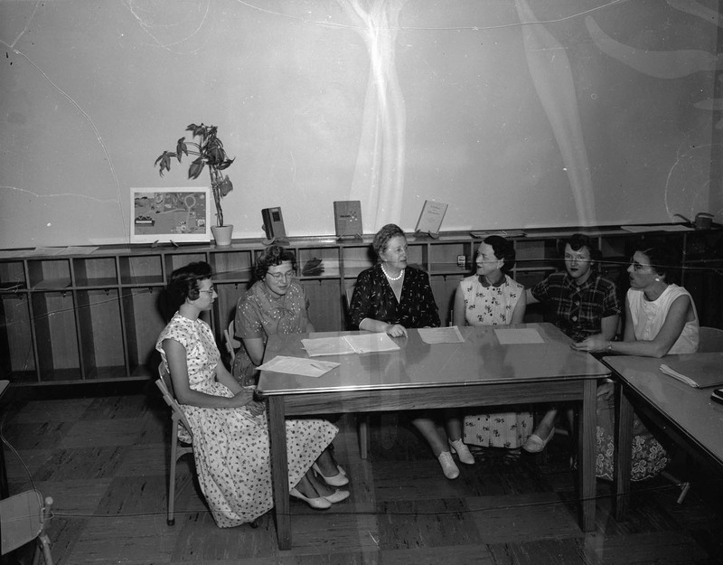 A group of women faculty sitting around a table discussing, documents can be seen in the table.