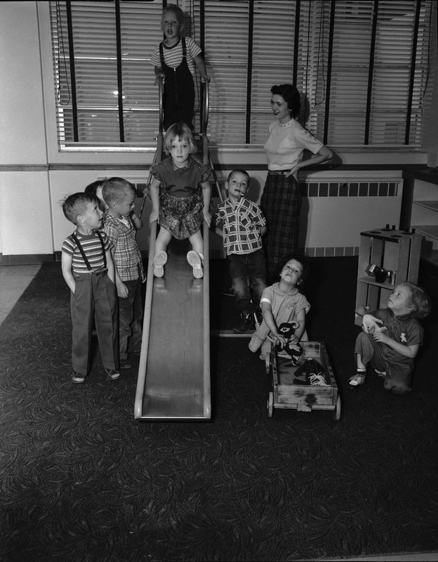 A woman looking after children as they go down an indoor slide.