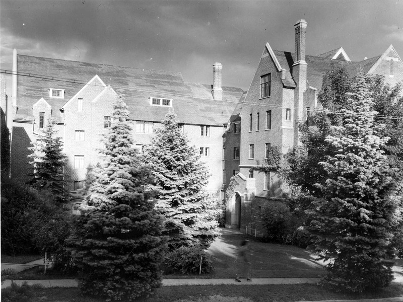 A photograph of Hays Hall, a five story brick and concrete building, built in 1926 as a women's dormitory. A woman can be seen walking in the foreground.