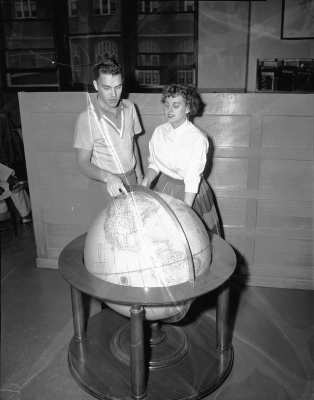 Two students looking at a large globe and pointing to an area in Canada.