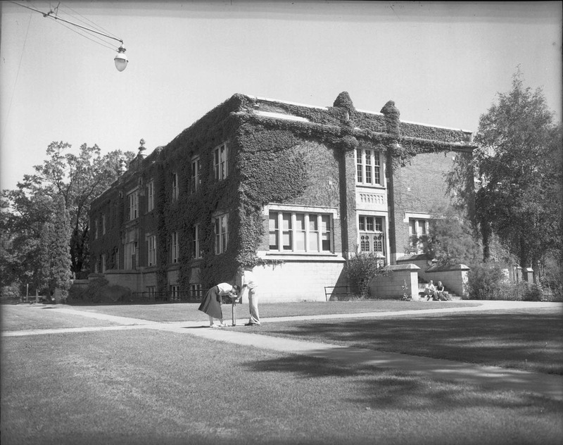 A photograph of the Student Union Building, covered in ivy. Two people can be seen in the foreground getting a drink of water.