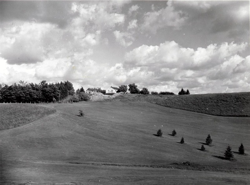 A photograph of the University of Idaho golf course. A tree line and house can be seen in the background.