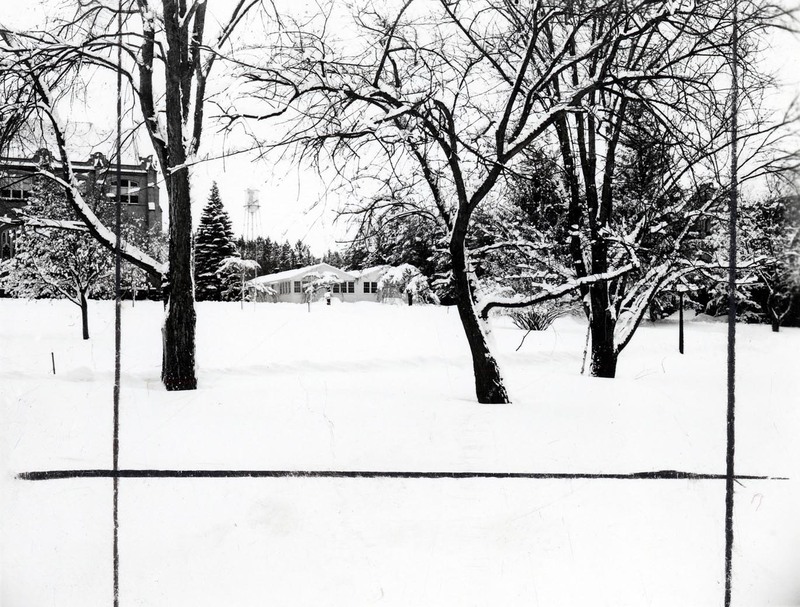 A snowy field with trees on University of Idaho campus, institutional buildings and the U of I watertower can be seen in the background. Black lines bisect the image.