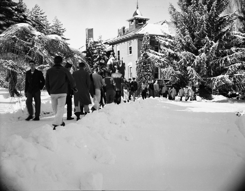 A large number of students walking along a snowy path between buildings.