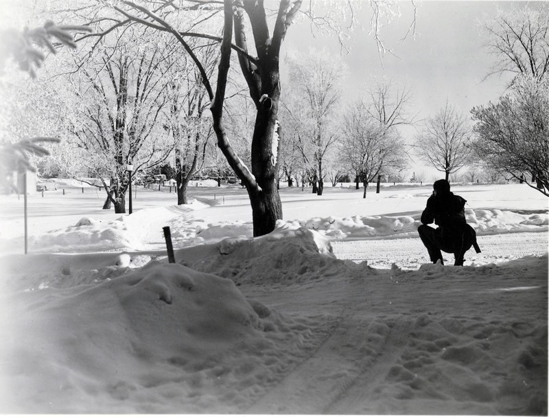 A person squatting on a snowy path through the Administration lawn during winter.