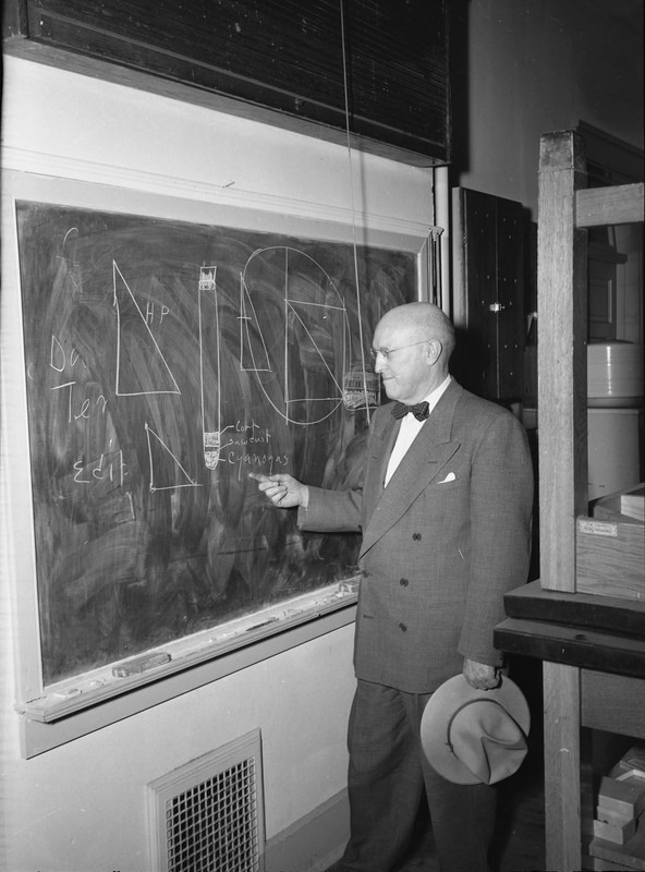 A photograph of University of Idaho President D.R. Theophilus writing on a blackboard with a hat in his hand.