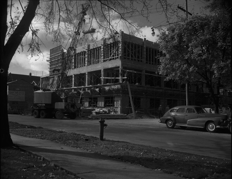 A photograph of the Student Union Building's 1950 addition under construction from across the street, showing a crane and automobile on the street.