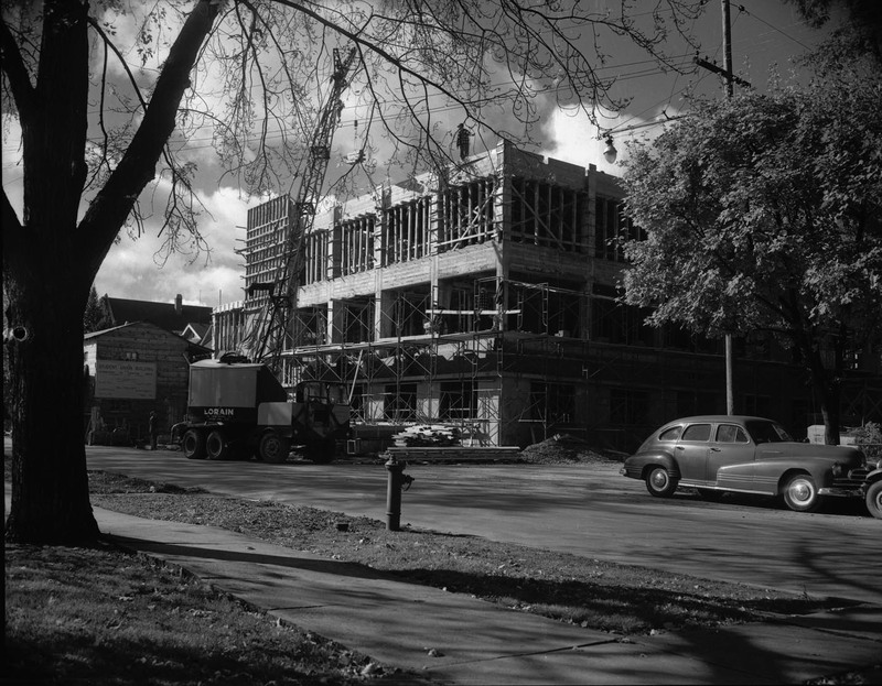 A photograph of the Student Union Building's 1950 addition under construction from across the street, showing a crane and automobile on the street.