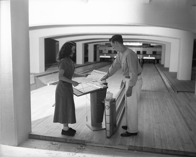 A photograph of two students in the Student Union Building bowling alley looking at a score sheet.