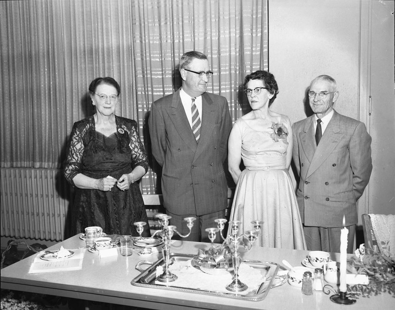 University of Idaho President J.E. Buchanan posing with two women and a man behind a table with candleholders, plates, and cups.