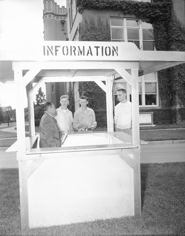 A photograph of new students standing at an information kiosk outside.