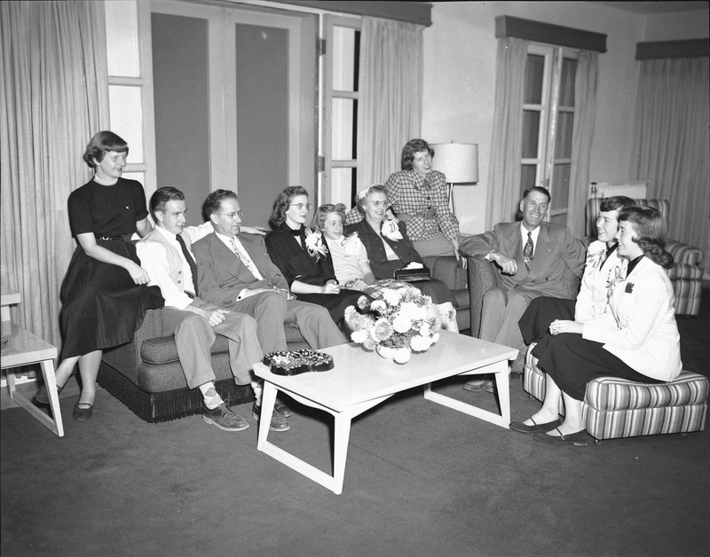 A group of people sit on a couch and some armchairs in conversation.