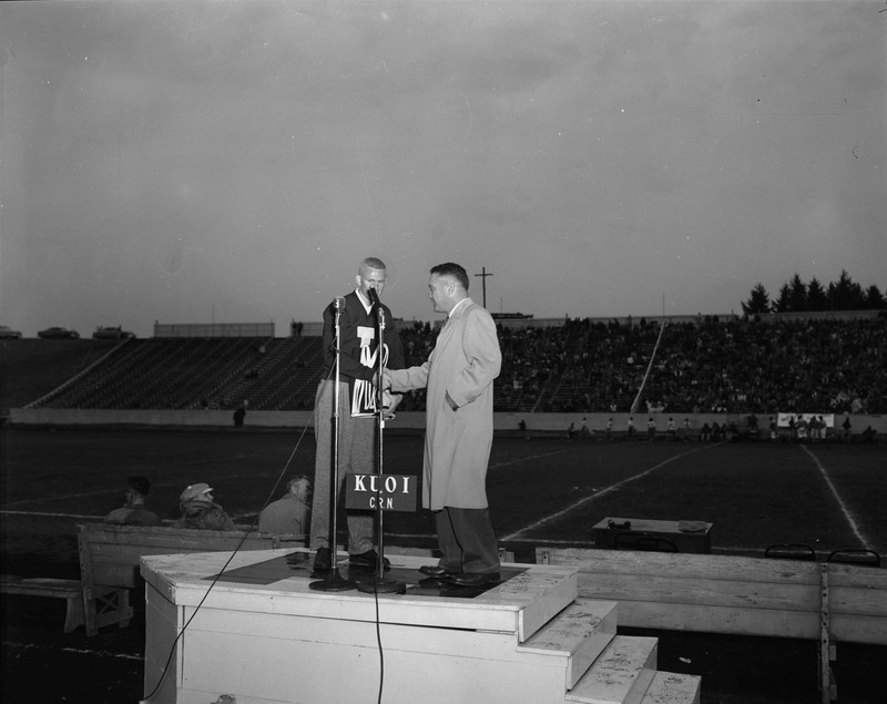 Two people shake hands on a podium at the Homecoming game.