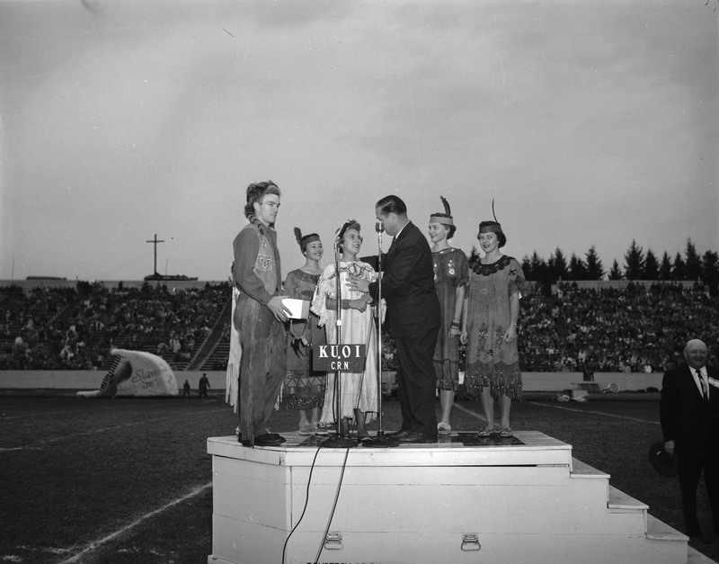Governor Smylie at the Homecoming game, speaking surrounded costumed students in the football stadium.
