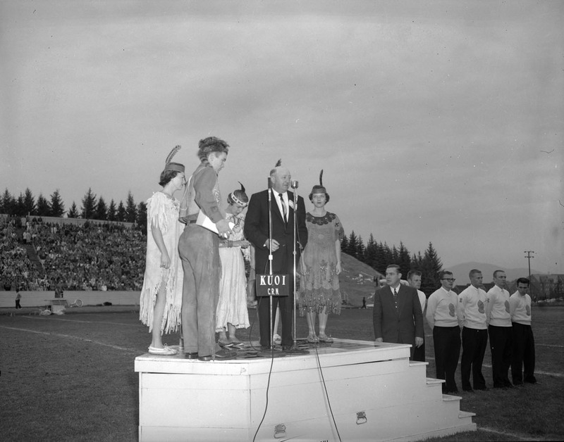 An unidentified man speaking surrounded costumed students in the football stadium.