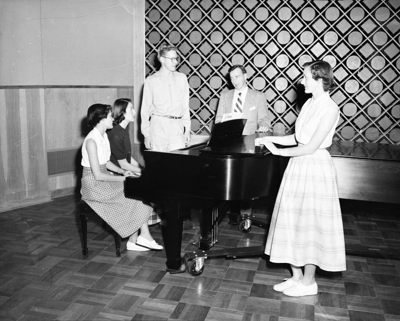 The Vandaleers, University of Idaho's singing group, practicing at a piano.