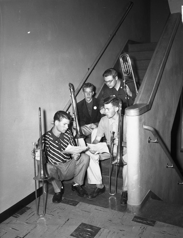 Student trombone players sit in a stairwell.