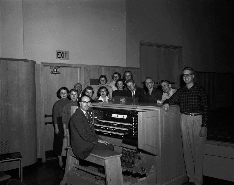 Choir practice being led by Music Department faculty Hall McInTyre Macklin at his three tier piano.