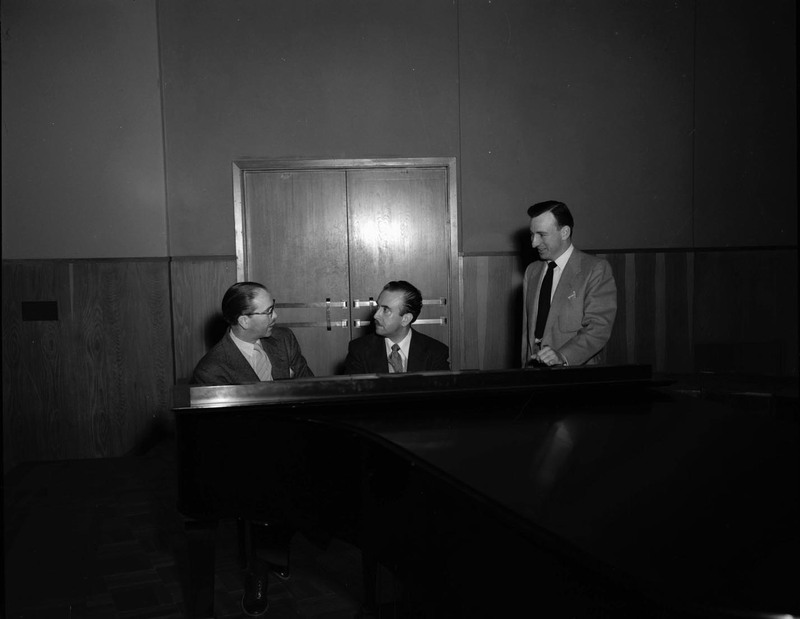 Hall Macklin, Glen Lockery and an unidentified man sit behind a piano