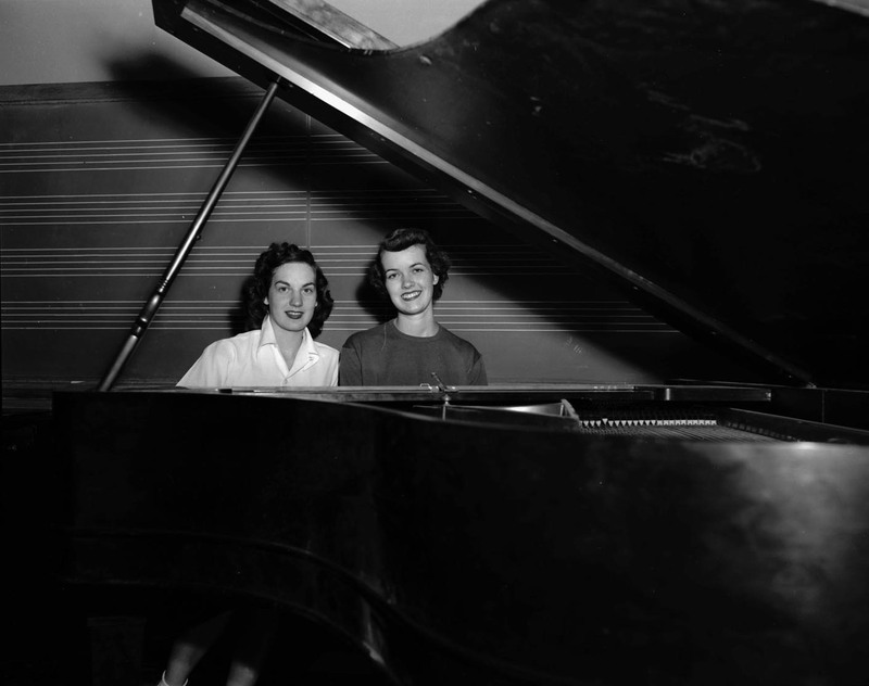Music students Phyllis Grocke and Jane Bostic sitting at a piano in front of a blackboard, both former Miss Idaho.