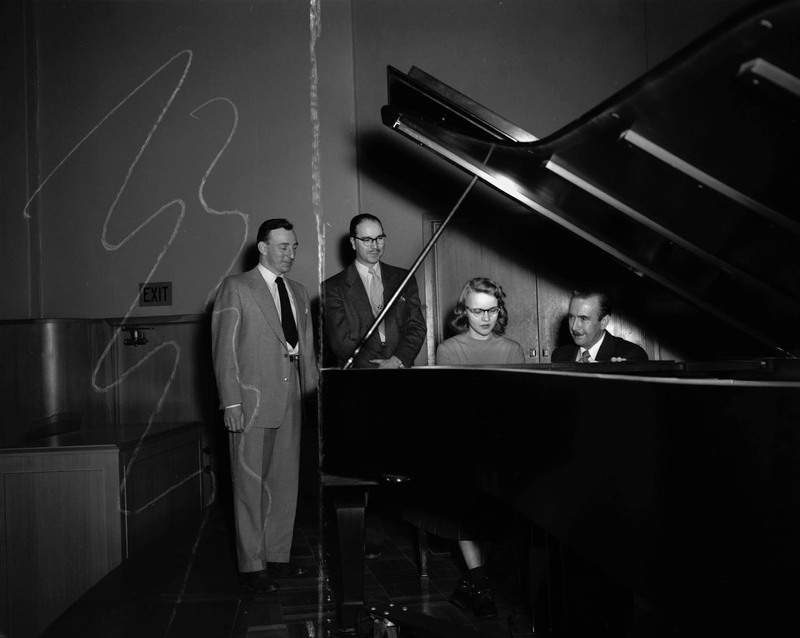 Hall Macklin and Glen Lockery watching two unidentified individuals play the piano.