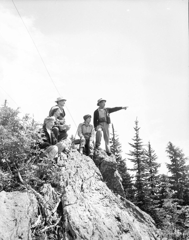 Students in a summer hiking class at the top of a boulder, pointing to something in the distance.