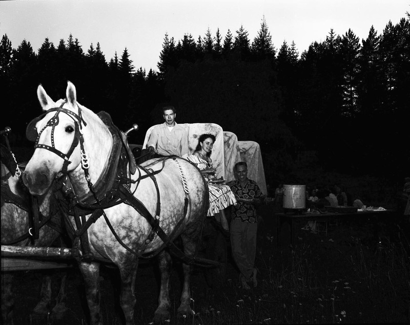 Students sitting posing with horses hitched to a wagon.