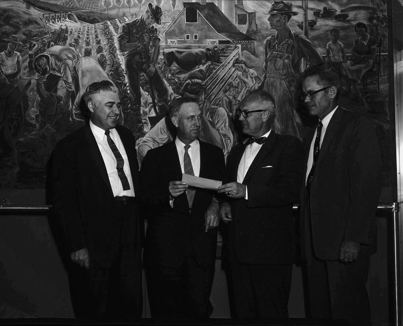 Left to right: J.W. Kipper, Dean James Kraus, Joe McArthur, and Associate Dean Don Marshall receiving a check in front of the Kirkwood mural in the Agricultural Science Building.