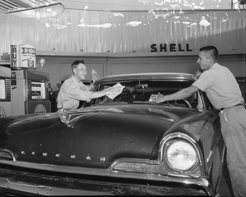 Gerald and Leonard Wunderlich running a gas station to pay their way through school, wiping off an automobile windshield with a "Shell" sign in background.