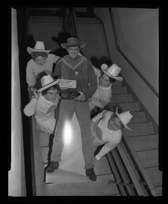 A photograph taken from above in a SUB stairwell of four members of the Spurs (l-r) Sharon Lance, Linda Smith, Katherine Koelsch, and Blanche Blecha carrying a cut out of Gunsmoke Star, James Arness that was used during the Idaho Cattlemen's Association meeting.