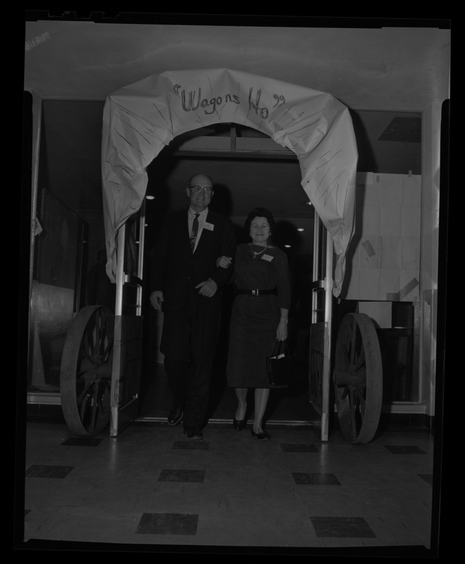 A man and women walk arm in arm through a doorway decorated to look like a cattle wagon with a sign that read "wagons ho!" for the Idaho Cattlemen's Association meeting.