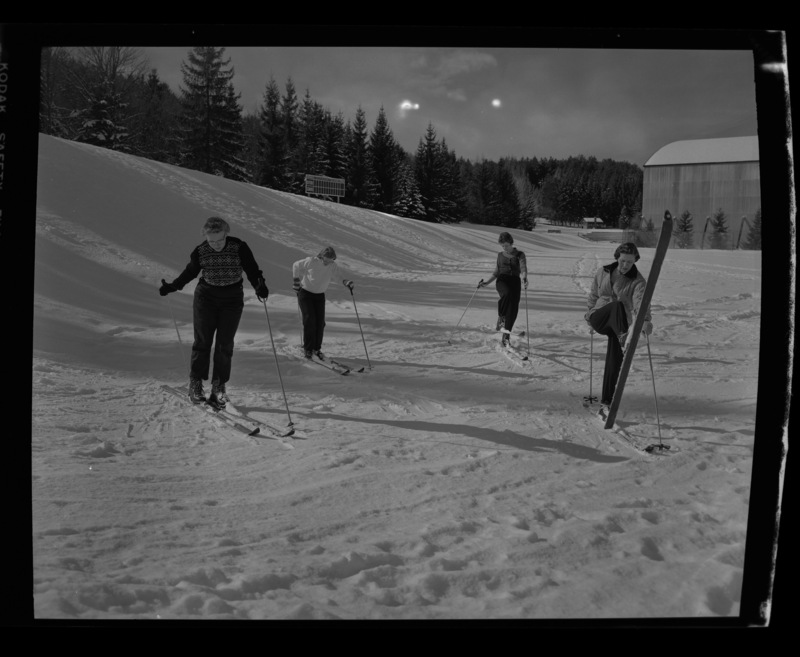 Four women with skiis on out in the snow in MacLean Field as a part of the University of Idaho women's ski club. The Field House can be seen in the background.