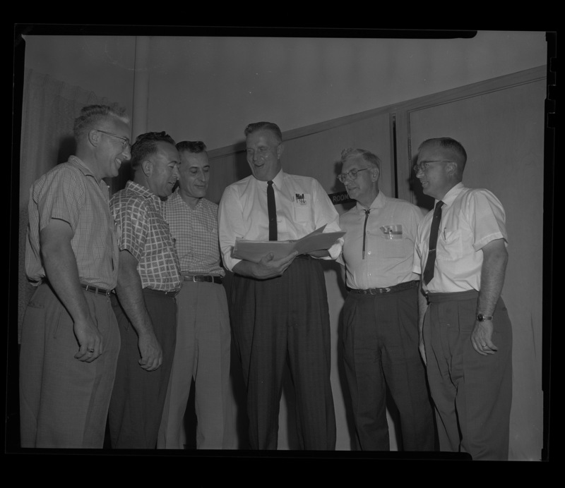 Six men stand together looking over a binder at the Idaho's Grocer's Conference at the University of Idaho.