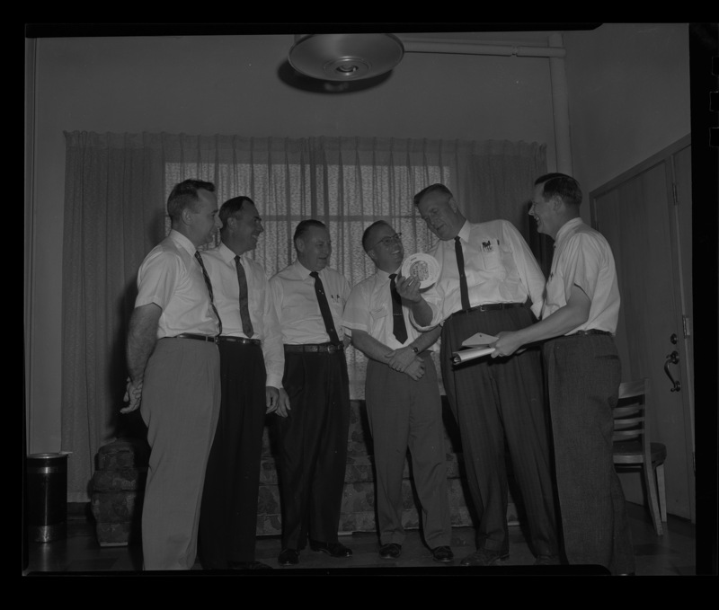 Six men stand together holding a Pet Milk Co. circle ruler at the Idaho's Grocer's Conference at the University of Idaho.