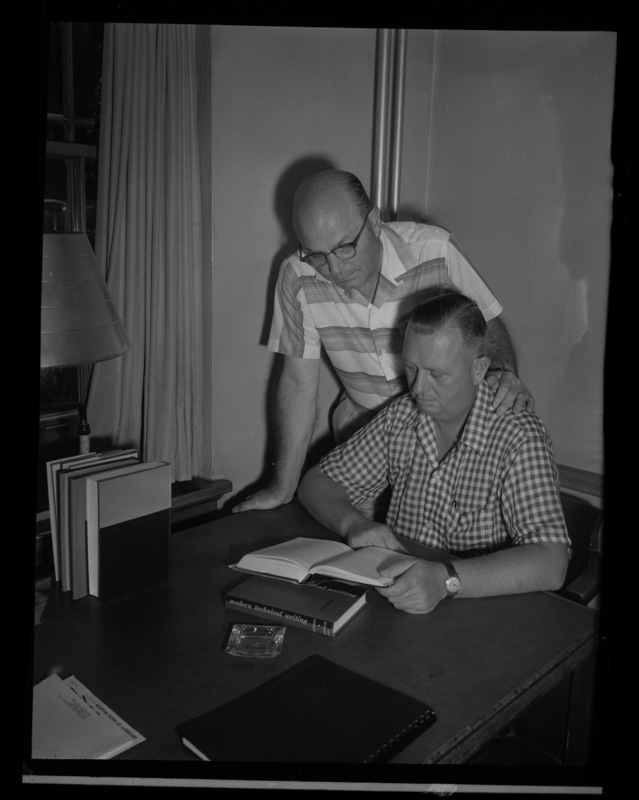 Two men read a book on modern technical writing for the Public Utilities Executive course held each summer.