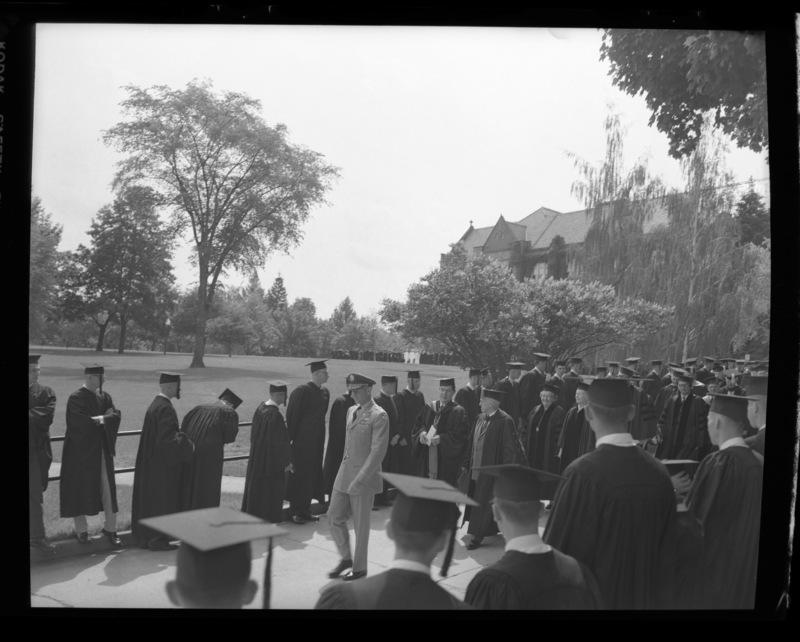 The Academic Parade leads the traditional commencement walk from the Administration Building to Memorial Gym. Behind the Military personnel is Governor Smylie (left) and President Theophilis (right).