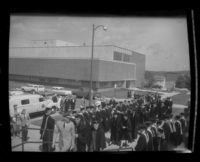 The Academic Parade walks up the stairs into Memorial Gym for Commencement. The Library building, greenhouses, and Ag Science building can be seen in the background.