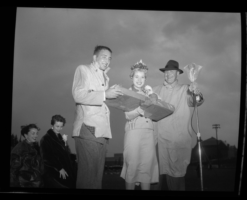 Homecoming queen Charmaine Deitz being crowned at the Homecoming Game by Dick Kerbs (left) and an unidentified man (right). (l-r) Tonia Peterson and Sharon Matheney, homecoming queen finalists, stand in the background.