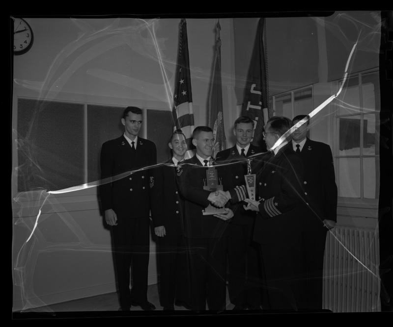 Captain G. F. Richardson (front, right) shakes hands with Ronald R. Shubert (front, left) while presenting the championship Navy rifle team with their trophies. In the back, from lef tto right: Roderick L. Mayer, Ray C. Shubert, Charles F. Bigsby, and Harold T. Barraclough.