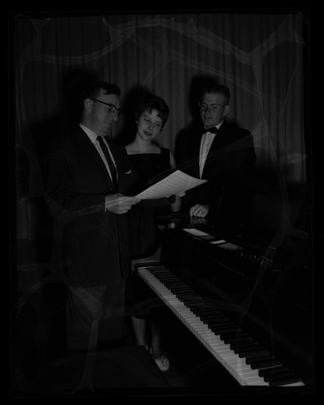 Music Professor Glen Lockery looking over music with Kris Madison (left) and Ardell Shockley (right) at a piano.
