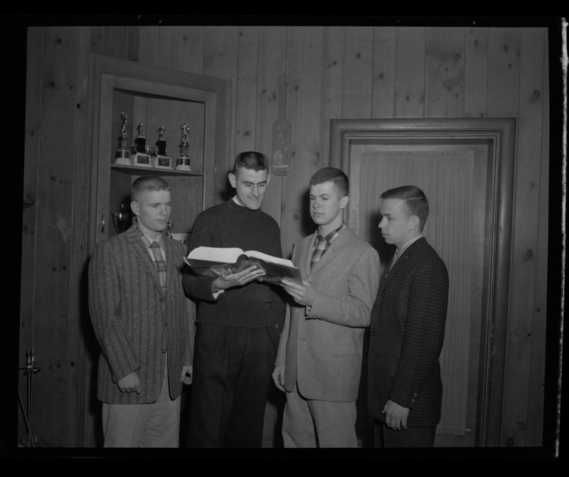 Members of Sigma Alpha Epsilon looking over a book in their fraternity house. From left to right: M.L. Gates, Pete Reed, Dave Briggs, David Stephenson.
