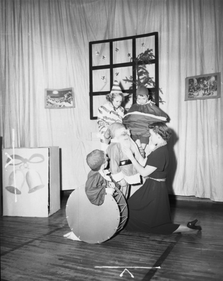 Woman helping young children into their Santa and elf costumes on the set of a play.