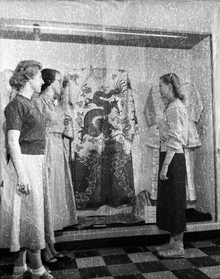 Three women examining an oriental garb with dragon imagery.